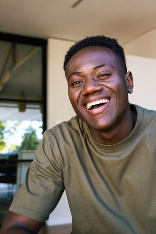 Smiling african man wearing olive tee and hoop earring enjoying sunlit patio moment