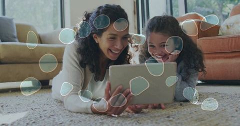 Mother daughter sharing tablet on cozy living room rug smiling and bonding