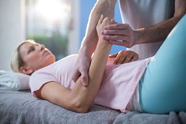 Female patient receiving hand massage from physiotherapist in a clinical setting. Ideal for use in healthcare, wellness, and rehabilitation content. Can be used to illustrate physical therapy, patient care, and therapeutic treatments.