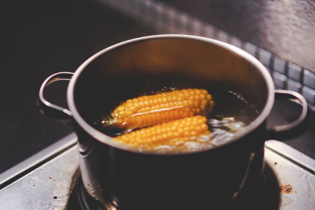 Corn on the cob boiling in a stainless steel pot on a stovetop. Great for culinary blogs, cooking tutorials, recipe websites, and food-related magazines to illustrate cooking techniques and food preparation.