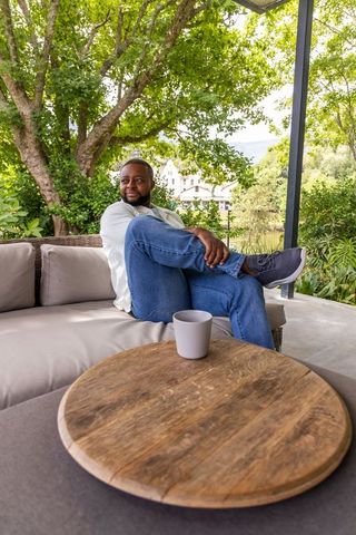 African man relaxing on patio sofa wearing light shirt and jeans with coffee mug