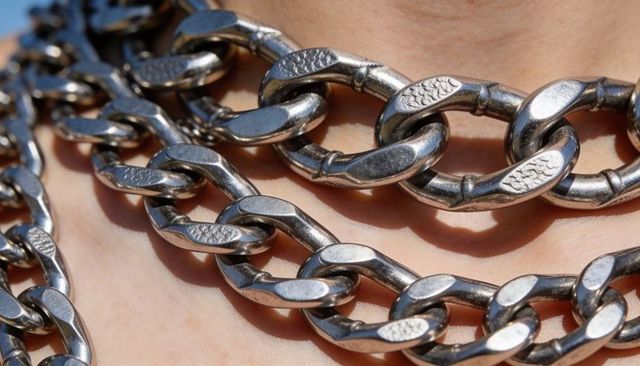 Heavy silver chain necklaces resting on bare neck and chest catching polished highlights