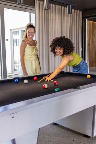 Diverse women playing pool in modern lounge laughing and leaning over black-felt table