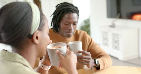 African American couple enjoying cozy hot drinks at home near fireplace cabinet