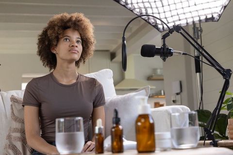 African american woman recording podcast in cozy home studio with amber skincare bottles