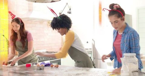 Friends baking together wearing reindeer headbands mixing batter on kitchen island