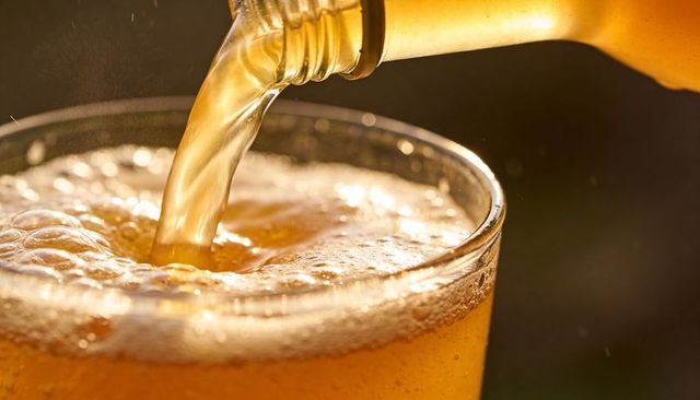 Pouring golden beer from brown bottle into glass with foamy head and sparkling bubbles