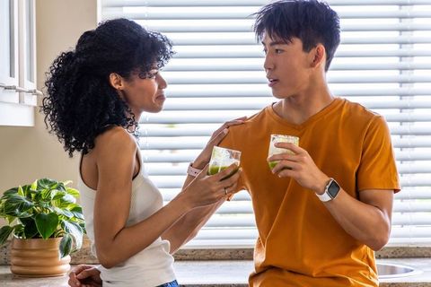 Young multicultural couple enjoying green smoothies at sunlit modern kitchen counter