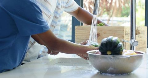 African american father and teen son rinsing vegetables together at kitchen sink