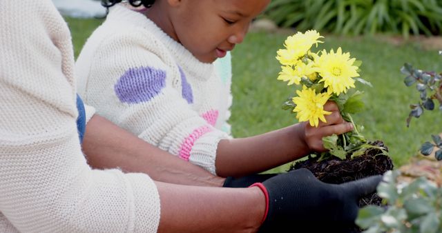 Mother and daughter engaged in gardening together, planting bright yellow flowers in a lush green backyard. This image can be used for promoting family activities, outdoor pastimes, gardening tutorials, and advertisements for garden supplies or spring-themed campaigns.