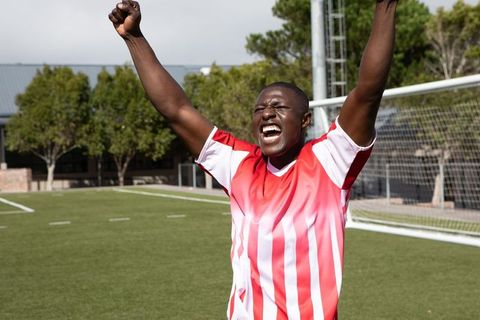 Athletic male footballer celebrating goal with raised arms on field