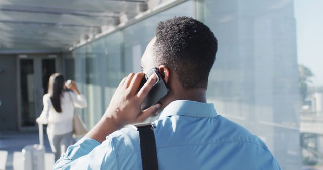 Professional businessman talking on phone outdoors in a modern urban setting. Perfect for depicting communication, business travel, and outdoor work environments. Useful for articles on modern technology, corporate lifestyle, urban living, and business communication.