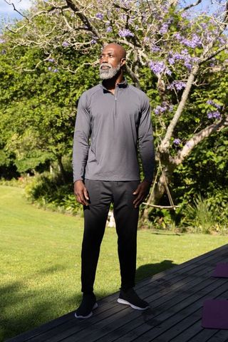 Mature african american man standing on deck in athletic wear with purple jacaranda blooms