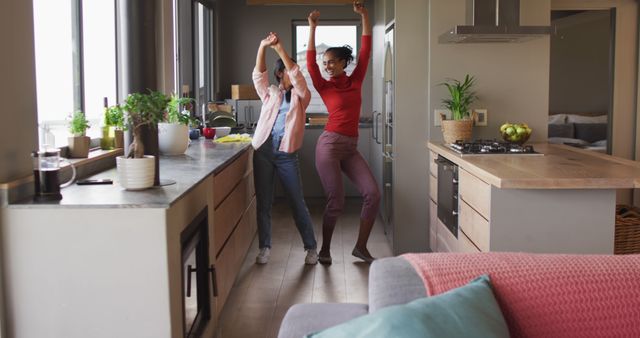 Image of happy biracial female friends having fun and dancing in kitchen. Friendship, having fun and spending quality time together at home.