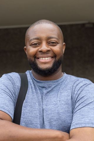 Confident smiling african man posing with arms crossed wearing blue t-shirt and bag strap