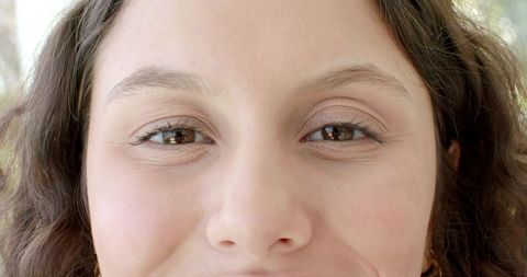 Sunlit closeup smiling young woman gazing into camera with brown eyes and hoop earring