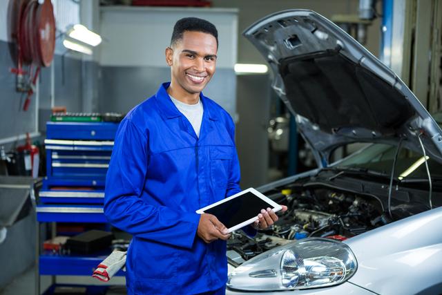 Portrait of happy mechanic using digital tablet at repair garage