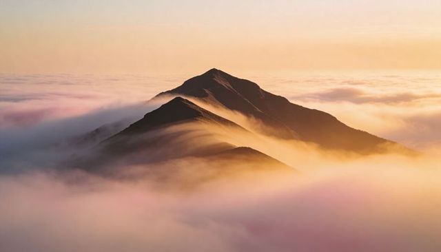 Sunlit mountain ridge rising through misty sea of clouds at golden hour, aerial alpine panorama