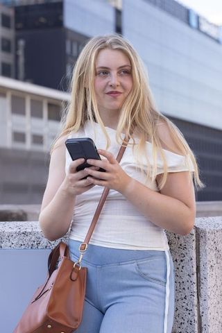 Young woman using smartphone while leaning on urban parapet wearing white off-shoulder top