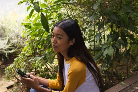 Asian Woman Enjoys Relaxing Moment in Lush Garden Holding Smartphone