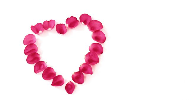 Rose petals are arranged in a heart shape on a white background, with copy space. This arrangement is often associated with romance and special occasions like Valentine's Day or anniversaries.