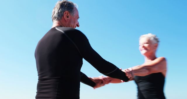 A senior Caucasian couple enjoys a playful moment together against a clear blue sky, with copy space. Their laughter and energy convey a sense of joy and vitality in their golden years.