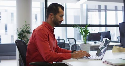 Focused professional typing on laptop in modern office setting