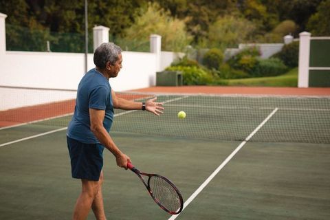 Senior man serving tennis ball on sunny outdoor court