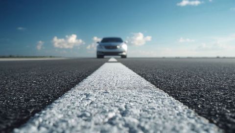 White centerline leading toward horizon with approaching silver sedan on open highway