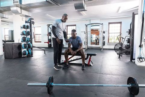 African American Trainer Coaching Client Using Tablet in Bright Functional Gym Interior