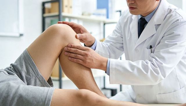 Doctor examining knee joint during orthopedic assessment in clinic with patient in gray shorts