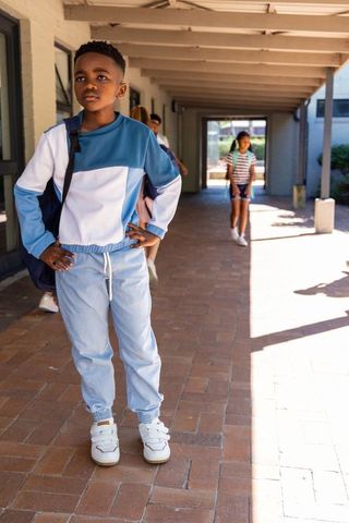 Confident african american preteen boy standing hands on hips on sunny campus walkway with backpack