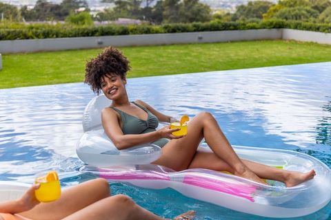 Relaxing on inflatable pool loungers, diverse friends holding citrus drinks, summer leisure