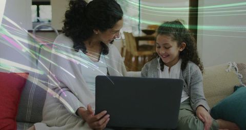 Mother and daughter learning together on laptop, smiling and bonding in living room