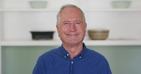 Smiling senior man wearing blue shirt standing in modern minimalist cozy home interior
