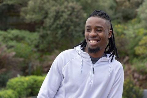Smiling african american man standing in garden wearing light gray zip-up hoodie