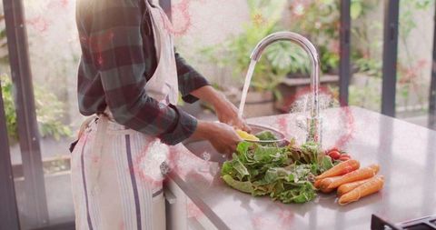 Washing fresh lettuce and vegetables at kitchen sink with stainless faucet, apron