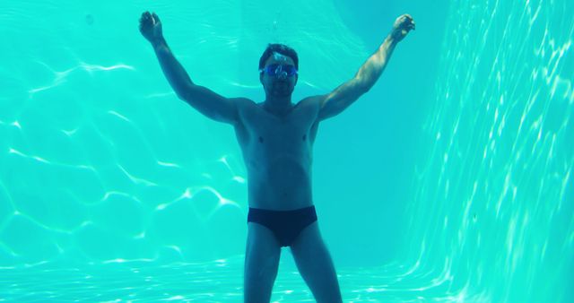 Man swimming underwater in a pool, wearing goggles and swim trunks. Ideal for use in content about fitness, swimming techniques, water sports, and healthy lifestyles. Perfect for illustrating aquatic activities and summer swimming experiences.