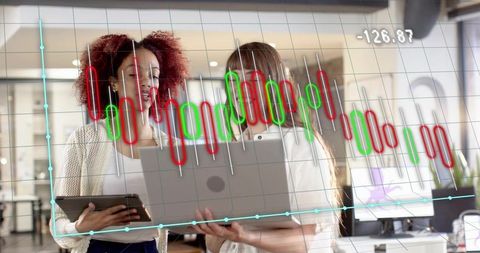 Coworkers reviewing stock candlestick chart on laptop and tablet in bright office