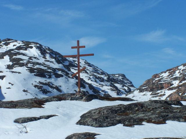 Depicting a cross in a rugged snowy mountain environment, this image exudes tranquil, spiritual and remote themes, perfect for webpages about religion, serenity, winter travels or mountain adventures. Suitable for illustrating the timeless natural beauty juxtaposed with human-made religious symbols.