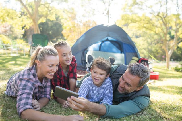Family enjoying a camping trip, taking a selfie together outside their tent. Ideal for use in advertisements, travel brochures, family-oriented products, and articles about outdoor activities, family bonding, and vacations.