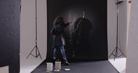 African american artist painting abstract splatter on black backdrop in creative studio