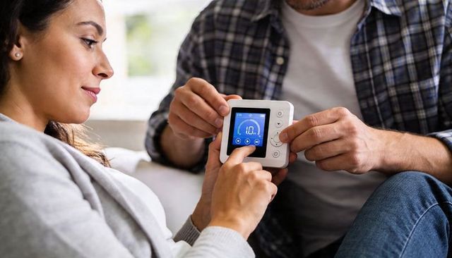 Couple adjusting smart thermostat on couch showing digital display for home comfort