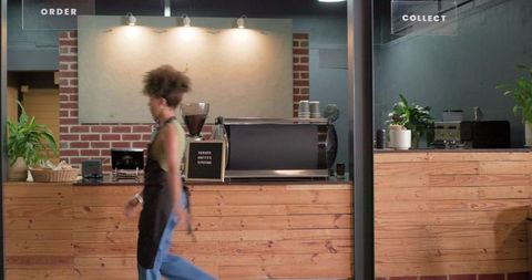 African american barista walking past wooden counter with espresso machine in urban cafe