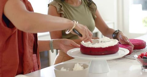 Two people decorating red velvet cake in bright home kitchen