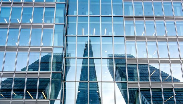 Reflective glass facade mirroring central spire and flanking skyscrapers in city