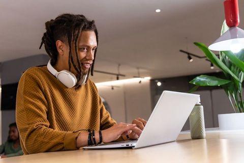 Creative professional working on laptop in modern coworking space with headphones