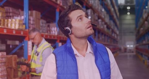 Warehouse Supervisor Wearing Headset and Checking Inventory on High Industrial Racks