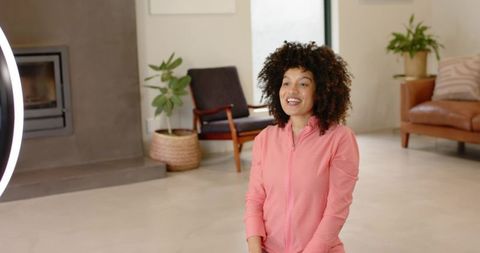 Woman speaking on camera in pink zip-up sitting on floor for living room interview