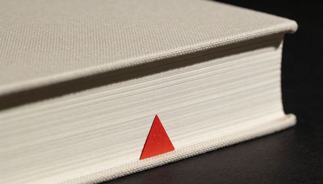 Minimal hardcover book fore-edge with red triangular tab and textured beige cloth binding